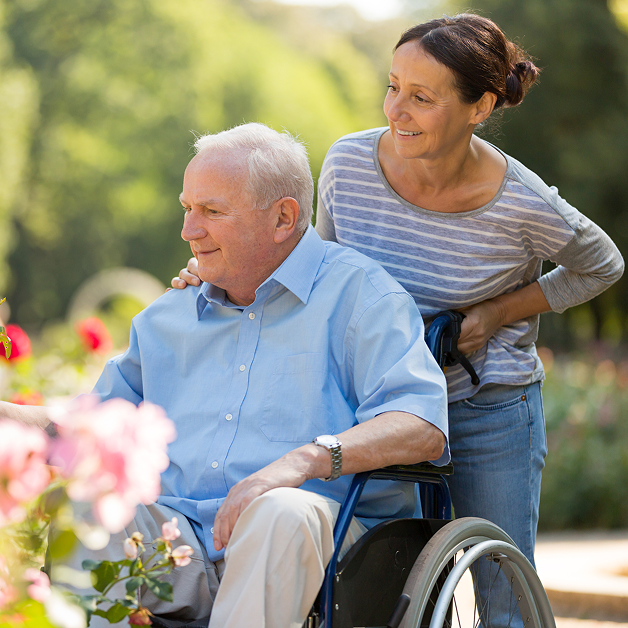 A senior man smiling while a caregiver assists him in the garden in Alabama
